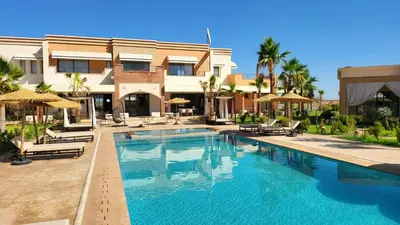 a swimming pool with chairs and umbrellas next to a building at Hôtel Jardins de lina et lea in Marrakech