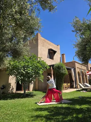 a woman sitting on a mat in front of a house at Villa Ily Marrakech Oasis privée avec piscine chauffée et panorama Atlas in Marrakech